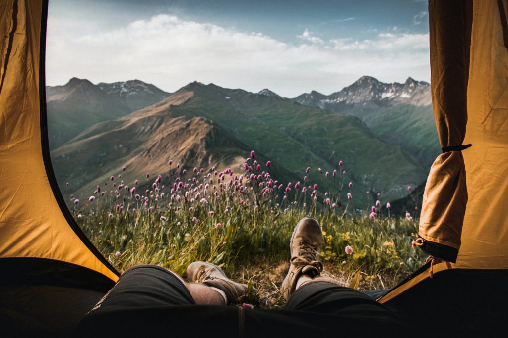 A person with hiking shoes laying in a tent with a view of mountains